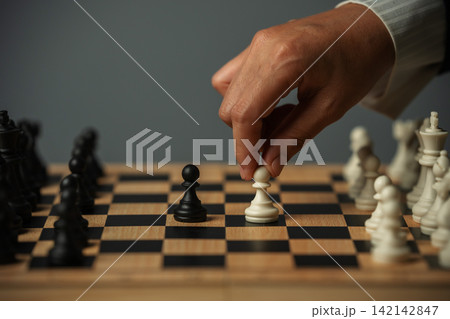 business hand moving a white pawn on wooden chessboard, strategy business hand moving a white pawn on wooden chessboard, strategy 142142847