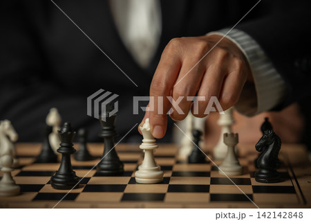 business hand touching a white queen chess on wooden board 142142848
