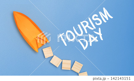 Origami boat on a blue background with wooden blocks and "Tourism Day" text, representing travel and adventure. Tourism Day Concept 142143151