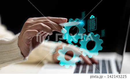 A woman hand using a stylus to interact with glowing blue virtual gears and document icons over a laptop, representing digital automation and workflow management. Data and automation concept 142143225