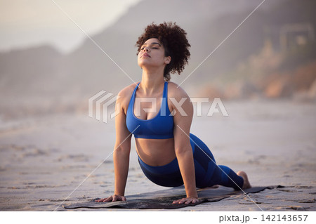 African woman, yoga and health for wellness at sea with peaceful mind, cobra pose and fitness. African person, zen and pilates workout at beach with stretching, spirituality and calm for mindset African woman, yoga and health for wellness at sea with peaceful mind, cobra pose and fitness. African person, zen and pilates workout at beach with stretching, spirituality and calm for mindset 142143657