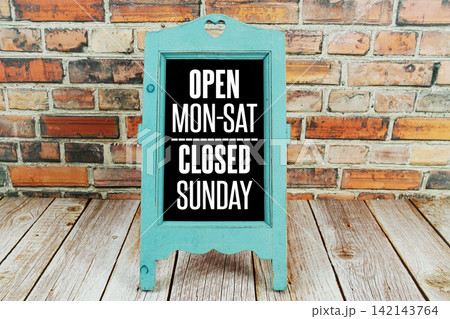 Open Monday to Saturday Closed Sunday text written on easel on wooden background Open Monday to Saturday Closed Sunday text written on easel on wooden background 142143764
