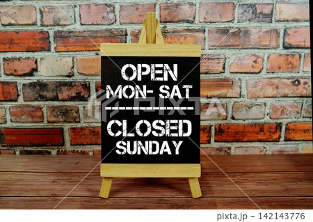 Open Monday to Saturday Closed Sunday text written on easel on wooden background Open Monday to Saturday Closed Sunday text written on easel on wooden background 142143776