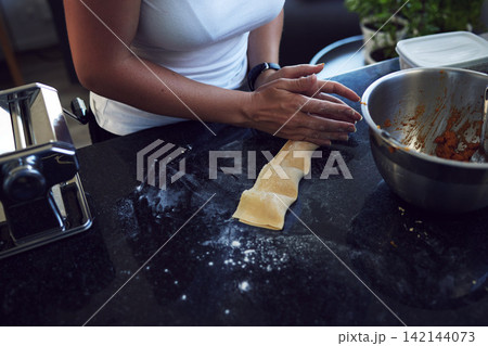 Person, hands and cooking pasta with mixing bowl on kitchen counter for healthy diet and nutrition at home . Woman, chef and food in closeup for handmade preparation of ravioli for balanced meal 142144073