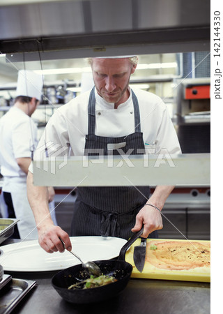 Man, chef and cooking food in kitchen with catering industry, nutrition and fine dining. Male employee, hospitality and gourmet cuisine for restaurant for tasting menu, plate and dinner in Germany Man, chef and cooking food in kitchen with catering industry, nutrition and fine dining. Male employee, hospitality and gourmet cuisine for restaurant for tasting menu, plate and dinner in Germany 142144330