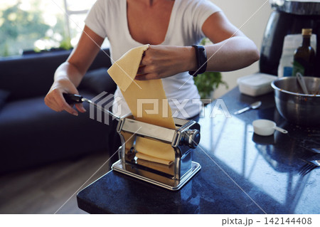 Woman, handmade pasta and prepare in kitchen with dough for spaghetti, ingredients and gourmet meal in home. Cooking, food and female person with machine for diy, dinner or recipe in apartment 142144408
