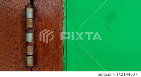 Worn metal hinges on a wooden door next to a bright green wall. Worn metal hinges on a wooden door next to a bright green wall. 142144637