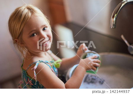 Kitchen, portrait and girl child washing dishes with smile, learning or help at basin in home. Housework, growth and kid cleaning at sink with development, pride and happy morning housekeeping chores Kitchen, portrait and girl child washing dishes with smile, learning or help at basin in home. Housework, growth and kid cleaning at sink with development, pride and happy morning housekeeping chores 142144937