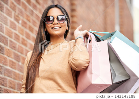 Portrait, shopping bag and woman in city happy on urban street for boutique, retail and clothing sale. Female person, sunglasses and smile outdoors with luxury products for fashionable rich customer 142145189