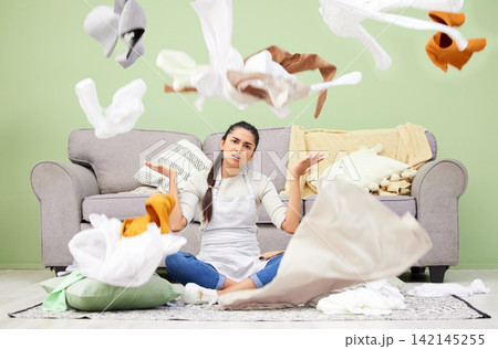 Woman, home and laundry with stress, chaos and portrait by sofa on floor in living room for hygiene. Frustrated girl, person and throw clothes on carpet, apron and cleaning with housework in lounge 142145255