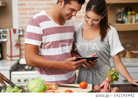 Cooking, tablet and couple learning in kitchen for healthy food or vegetables for lunch or dinner. Online, tutorial or romantic woman in meal prep for salad preparation or hungry vegan man in England Cooking, tablet and couple learning in kitchen for healthy food or vegetables for lunch or dinner. Online, tutorial or romantic woman in meal prep for salad preparation or hungry vegan man in England 142145442