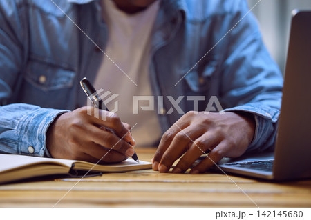 Man, hands and writing with laptop in book for studying, elearning or education on desk at home. Closeup of male person, student or writer taking notes in diary for reminder, information or agenda Man, hands and writing with laptop in book for studying, elearning or education on desk at home. Closeup of male person, student or writer taking notes in diary for reminder, information or agenda 142145680