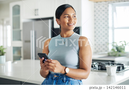 Cellphone, thinking and woman in kitchen networking on internet, mobile app or website at home. Technology, happy and young female person scroll online with phone by counter at modern apartment. 142146011