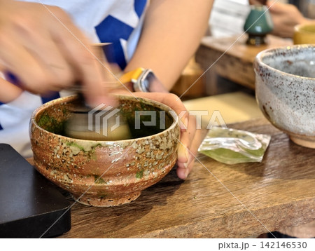 Close-up of a barista whisking green tea matcha powder in a ceramic bowl with motion blur. 142146530