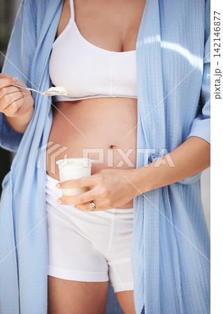 Pregnancy, belly and woman in home with yogurt for snack, craving and nutrition in bedroom. Pregnant person, abdomen and dessert or ice cream for vitamin, protein and wellness for tummy or stomach 142146877