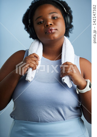 Woman, studio and headphone for portrait and towel, serious and blue background for workout goal. Confident, online streaming and music for fitness, audio or listening for body health and podcast Woman, studio and headphone for portrait and towel, serious and blue background for workout goal. Confident, online streaming and music for fitness, audio or listening for body health and podcast 142147382