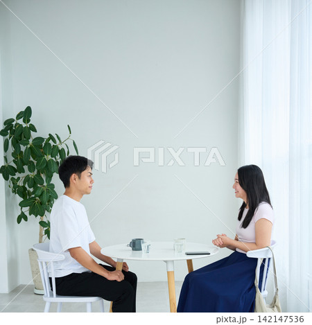 テーブルで向かい合って話す若い男女 テーブルで向かい合って話す若い男女 142147536