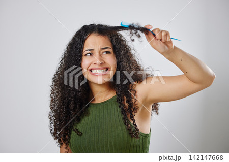 Messy hair, knot and scared woman with comb in studio for tangle, stress and problem on grey background. Curly, haircare and model with anxiety for brushing fail, damage or styling hairloss results 142147668