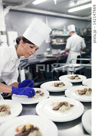 Cooking, chef and woman in restaurant kitchen with food on plate for fine dining, service or hospitality. Expert, culinary professional and worker preparing meal, lunch or dinner for hotel catering 142147669