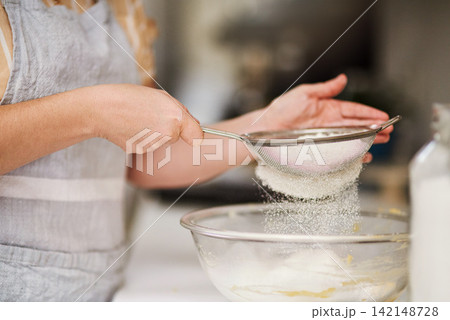 Woman, hands and sifting flour in kitchen for cookies, bread and breakfast ingredients in cafe. Female baker, cooking and dessert for bakery, small business and startup coffee shop or restaurant Woman, hands and sifting flour in kitchen for cookies, bread and breakfast ingredients in cafe. Female baker, cooking and dessert for bakery, small business and startup coffee shop or restaurant 142148728