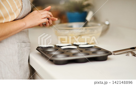 Baker hands, baking tray and cupcakes prepare in kitchen in house for relax or therapeutic hobby. Dessert, cooking and professional person with homemade for small business or home recipe with paper. Baker hands, baking tray and cupcakes prepare in kitchen in house for relax or therapeutic hobby. Dessert, cooking and professional person with homemade for small business or home recipe with paper. 142148896