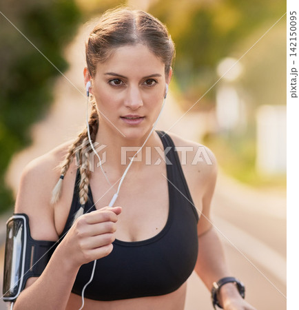 Woman, running and exercise for fitness with earphones or music in outdoor London. Female person, workout and active with smartphone for training or wellness with morning jog for wellbeing in street 142150095