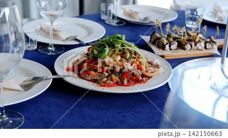 Warm salad with beef and vegetables is served on a festive table with a blue tablecloth, creating an inviting atmosphere for a celebratory meal 142150663