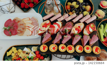 Catering professional arranging buffet spread with colorful appetizers, canapes, sandwiches, salads, fruits, and sweet desserts for event guests Catering professional arranging buffet spread with colorful appetizers, canapes, sandwiches, salads, fruits, and sweet desserts for event guests 142150664
