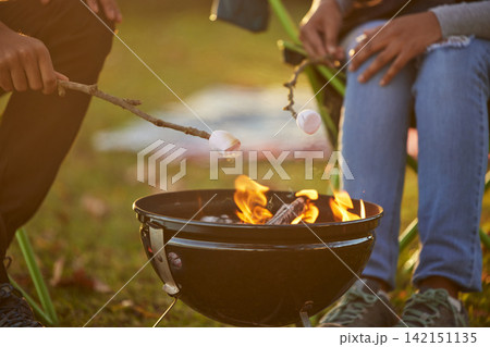 Couple, toasting and marshmallow by fire on camping in forest with love, bonding and memories for adventure. People, sweets and food for dessert by flame in nature on vacation or holiday on picnic 142151135