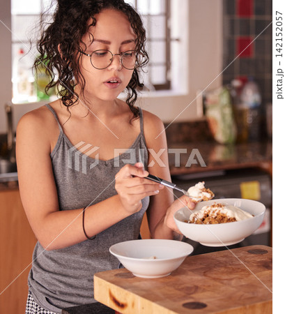 Girl, breakfast and bowl with diet in kitchen for nutrition, vitamins or food portion at home. Young teenager or female person in pajamas for morning meal, snack or eating cereal on table at house 142152057