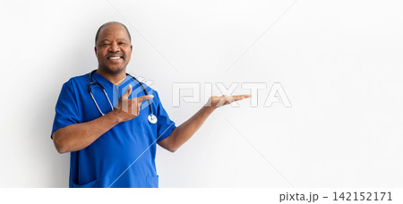 Smiling Black doctor in blue scrubs presenting copy space with open hand 142152171
