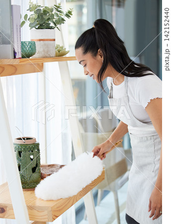 Duster, girl and cleaning dust in home for housekeeping, furniture and maintenance with hygiene. Woman, happy and dusting shelf for housework with brush in house, living room and work in hospitality. 142152440