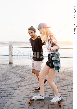 Couple, man and woman with skateboard on boardwalk, happy and helping for balance, learning and playful by sea. People, teaching and skating with support and fun on promenade for vacation in Italy Couple, man and woman with skateboard on boardwalk, happy and helping for balance, learning and playful by sea. People, teaching and skating with support and fun on promenade for vacation in Italy 142152942