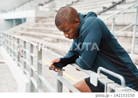 Stadium, athlete and black man with phone on social media, online chat or news on fitness on break. Typing, communication and runner in arena with smartphone for mobile app or internet notification 142153150