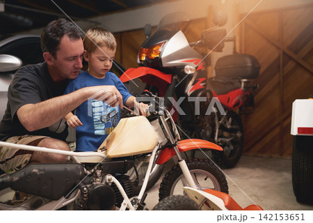 Parent, son and fixing with bike in garage at home for teamwork, support and repair with tools. Family, father and child for bonding, helping and together as mechanic for motorbike in carport 142153651