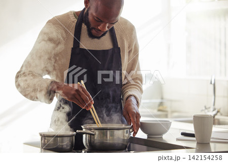 Man, cooking and pot with steam in the home for lunch or dinner, busy and hungry for food with preparation. Catering, African chef with chopsticks for Asian cuisine and meal with nutrition in kitchen 142154258