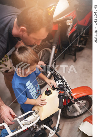 Dad, child and fixing with bike in garage at home for teamwork, support and repair with tools to educate. Family, father and son for bonding, helping and together as mechanic for motorbike in carport 142154548