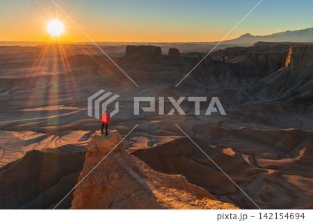 Peaceful solitary hiker standing on high rock cliff watching golden sunrise over vast desert canyon landscape in utah full of wonder 142154694
