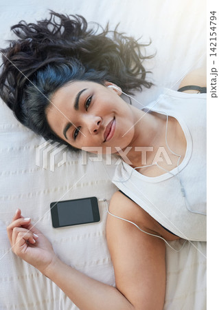 Woman, earphone and music in bed with cellphone, audio or rest in home. Calm, portrait and peace in bedroom for lazy day on weekend with podcast, comfortable and sleep or self care for female person Woman, earphone and music in bed with cellphone, audio or rest in home. Calm, portrait and peace in bedroom for lazy day on weekend with podcast, comfortable and sleep or self care for female person 142154794