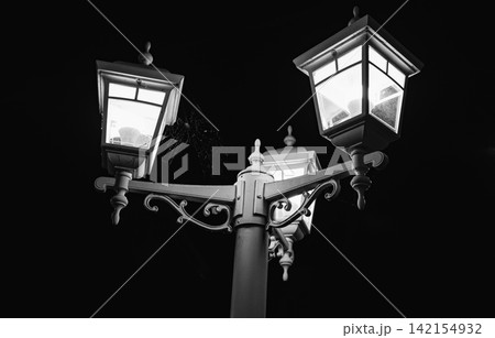 Vintage street lamp with three glowing lights at night, illuminated lantern against dark sky Vintage street lamp with three glowing lights at night, illuminated lantern against dark sky 142154932