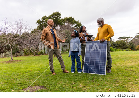 African American family with child teen senior in coats holding solar panel checking tablet in park African American family with child teen senior in coats holding solar panel checking tablet in park 142155315