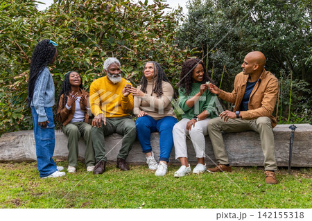 African American family sitting on wooden log bench in park passing small brown seeds in sweaters 142155318