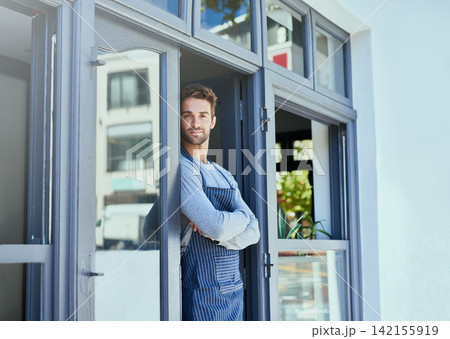 Door, crossed arms and portrait of waiter by coffee shop with positive, happy and confident attitude. Smile, pride and man barista standing by cafe or restaurant entrance for welcome in hospitality. 142155919
