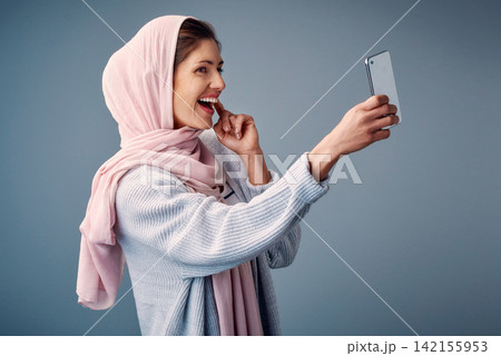 Islamic woman, selfie and influencer with smile, happiness and social media on grey studio background. Muslim person, model and girl with smartphone, content creation for culture, hijab and tradition Islamic woman, selfie and influencer with smile, happiness and social media on grey studio background. Muslim person, model and girl with smartphone, content creation for culture, hijab and tradition 142155953