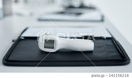 Medical, digital and thermometer gun in office of hospital with clipboard for data, information and record of patient symptoms. Document, clinic and equipment for safety check with healthcare Medical, digital and thermometer gun in office of hospital with clipboard for data, information and record of patient symptoms. Document, clinic and equipment for safety check with healthcare 142156218