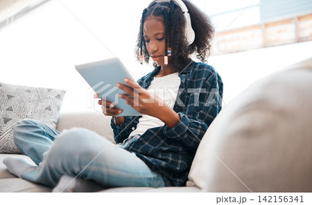 Digital tablet, black girl and headphones on sofa for elearning, education or learning in living room. Technology, person and teenager for streaming videos, play online games or relax in home Digital tablet, black girl and headphones on sofa for elearning, education or learning in living room. Technology, person and teenager for streaming videos, play online games or relax in home 142156341