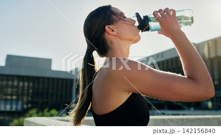 City, profile or woman drinking water on break in exercise, running workout or fitness training. Girl athlete, relax or thirsty sports runner with liquid bottle for wellness or hydration in England City, profile or woman drinking water on break in exercise, running workout or fitness training. Girl athlete, relax or thirsty sports runner with liquid bottle for wellness or hydration in England 142156840