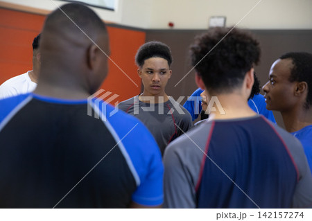 African American teenage males huddling in gymnasium, teen wearing grey athletic top with red seams African American teenage males huddling in gymnasium, teen wearing grey athletic top with red seams 142157274
