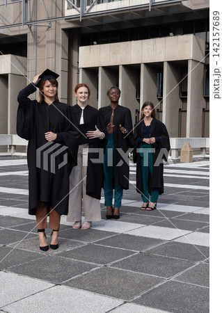 Diverse female graduates posing on tiled campus plaza wearing black gowns and adjusting mortarboard 142157689