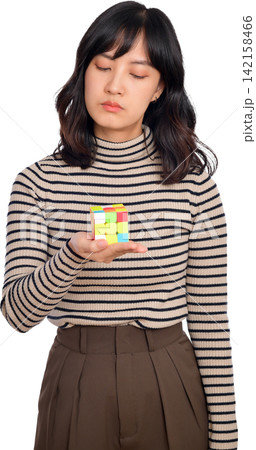 Asian woman holding colorful cube with thoughtful expression in striped sweater and brown skirt Asian woman holding colorful cube with thoughtful expression in striped sweater and brown skirt 142158466